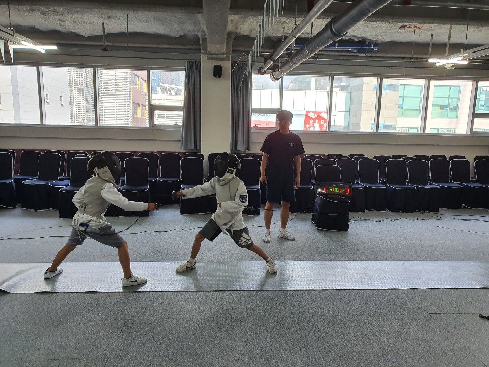 An ICS student in fencing gear during a competitive bout, fencer in white uniform with mask.