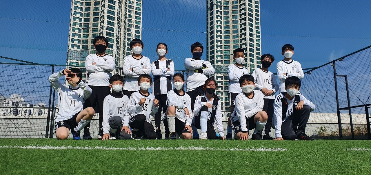 The ICS soccer team posed on a turf field, players in numbered jerseys with apartment towers in the background.